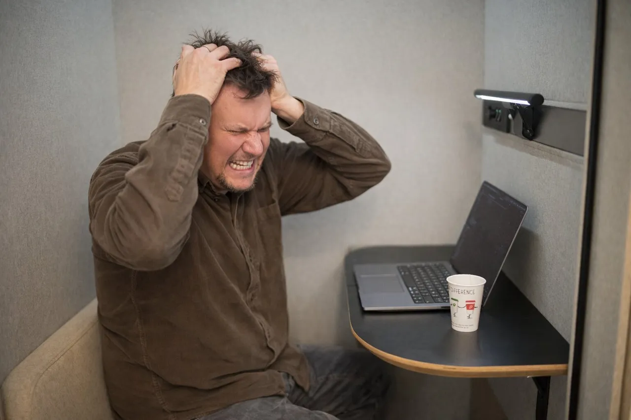 Gefrustreerde medewerker met de handen in het haar achter een laptop in een werkcabine